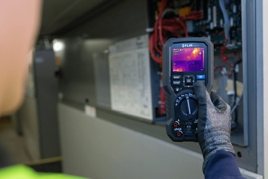 Engineer using a FLIR thermal-imaging multimeter on commercial equipment